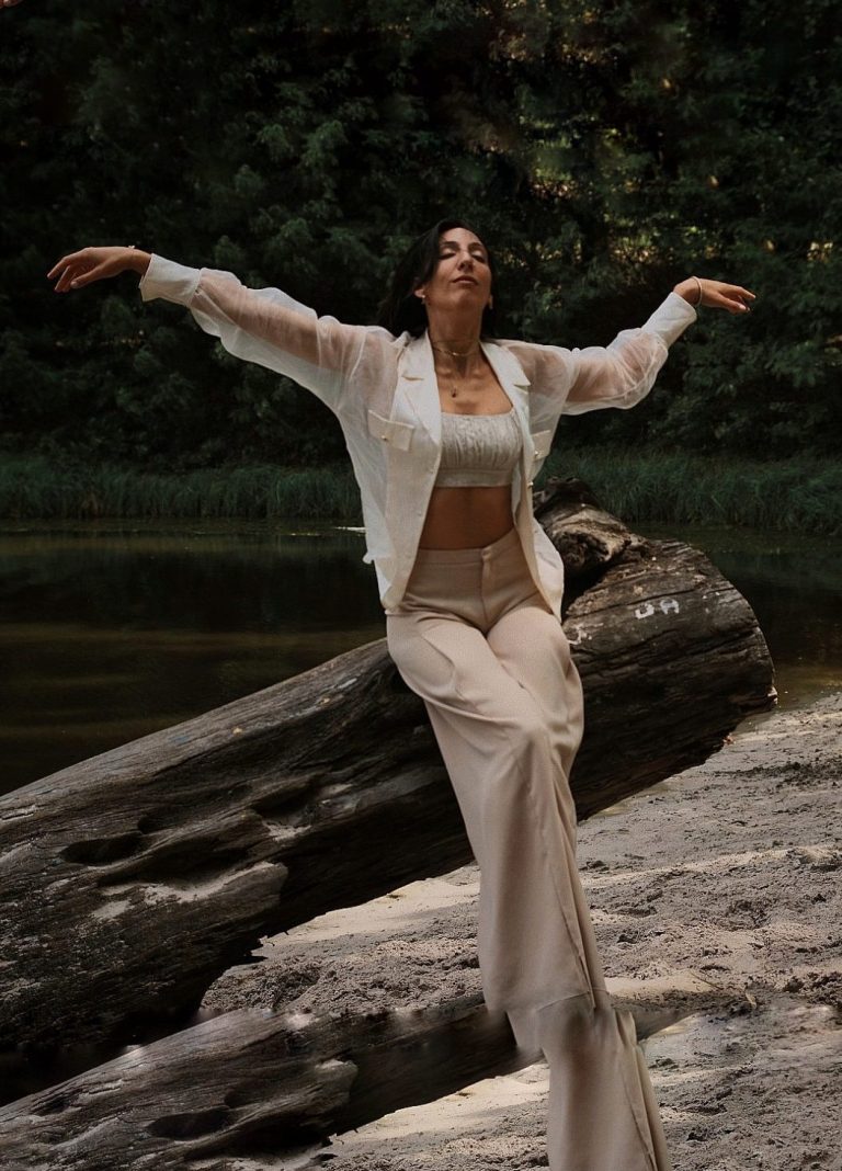 Frau sitzt frei verbunden und kraftvoll auf Baumstamm,Transformation, Entwicklung, spirituell, Coaching, Achtsamkeit, Sinnlichkeit, Trauma, Breathwork Junge Frau sitzt entspannt aber kraftvoll auf einem Baumstamm am See. Die Arme sind frei und genießerisch nach oben gestreckt, Augen zu.