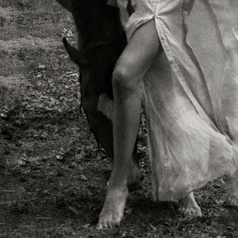Eine Frau im langen Kleid steht barfuß neben einem grasenden Pferd, Raffaela Richter Gohr, Untamed, Ungezähmt, Wild, Natur, Verbindung, Entwicklung, Trauma, Heilung, Breathwork, Coaching, Männerarbeit, Frauenarbeit, Embodiment Eine Frau im langen Kleid steht barfuß neben einem grasenden Pferd.